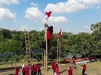 A group of people climbing a ladder to place an Indonesian flag at the top during an outbound team-building challenge.