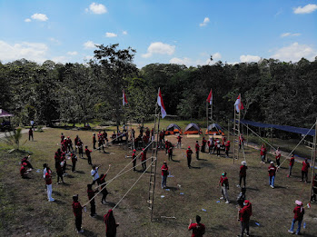 A wider view of a group engaged in an outdoor game, with participants climbing a ladder and placing an Indonesian flag at the top.