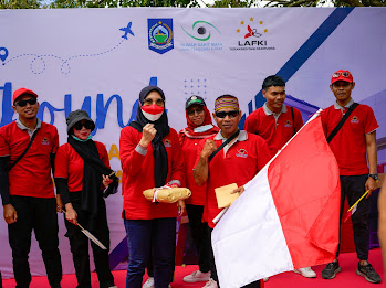 A leader in red clothing delivering a speech and holding an Indonesian flag during a outbound team-building event.