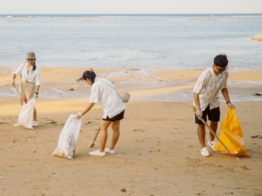 Three people cleaning plastic waste from a beach as part of a CSR initiative.