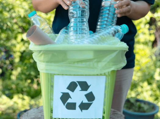 A person disposing of plastic bottles into a recycling bin marked with a recycling symbol.
